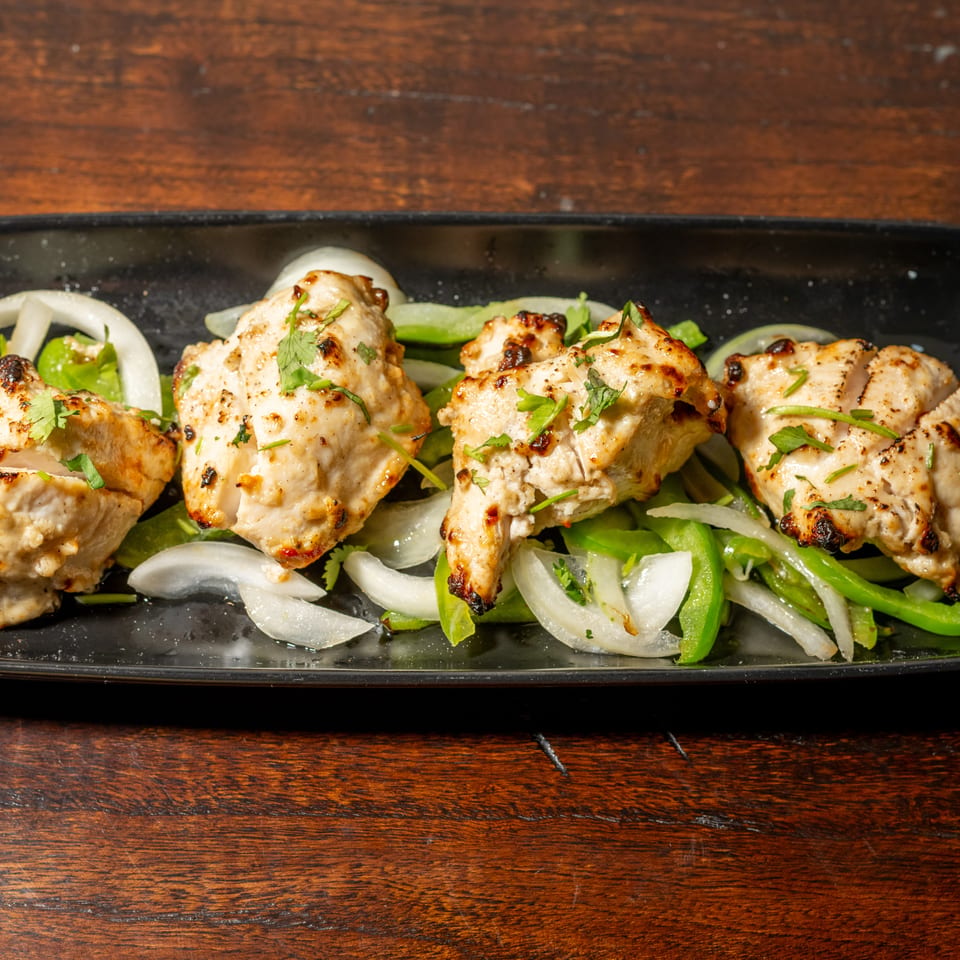 Grilled chicken tikka pieces with charred edges, garnished with cilantro, onions, and green peppers.