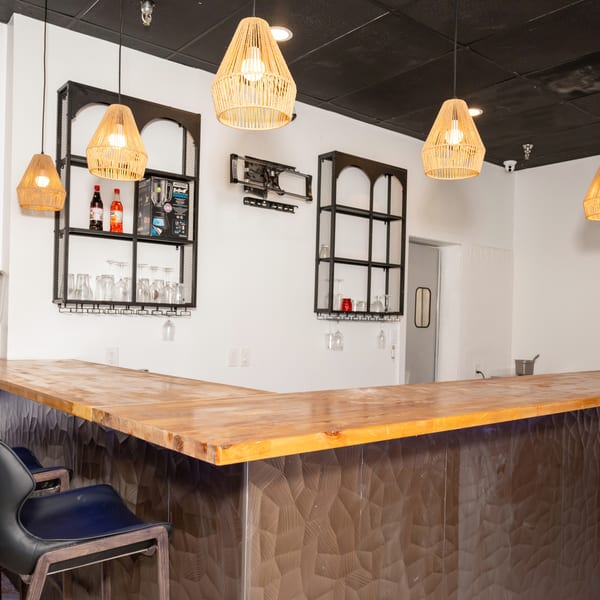 A modern bar area with a wooden countertop, black textured base, and wicker pendant lights.
