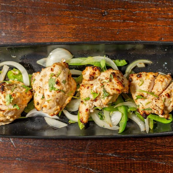 Four pieces of grilled chicken tikka with onions and green peppers on a black plate.