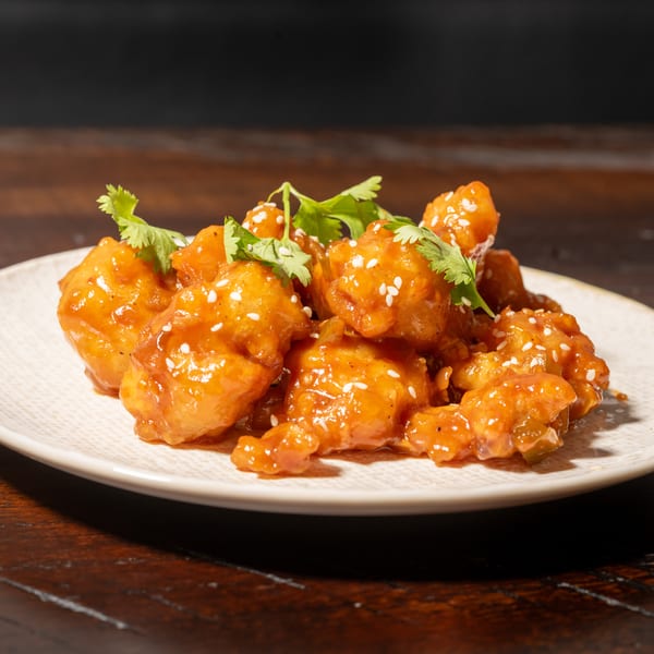 Orange chicken with sesame seeds and cilantro on a white plate, on a dark wooden table.