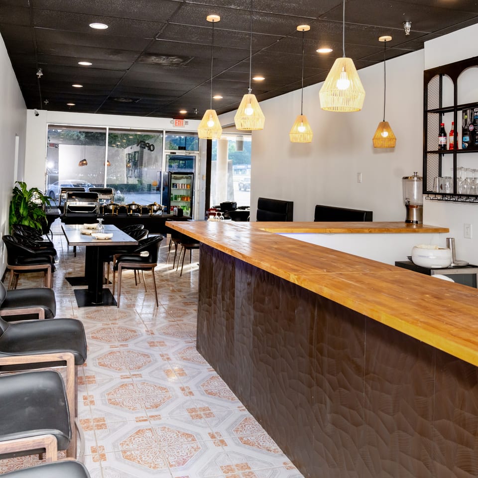 Modern restaurant interior with a wooden bar, black chairs, and patterned floor tiles.