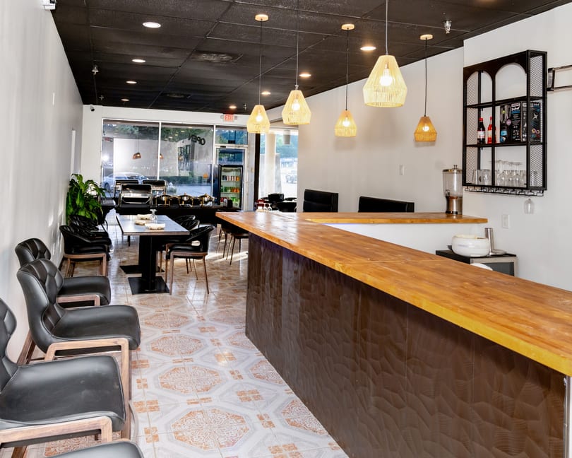 Modern restaurant interior with a wooden bar, black chairs, and patterned floor tiles.