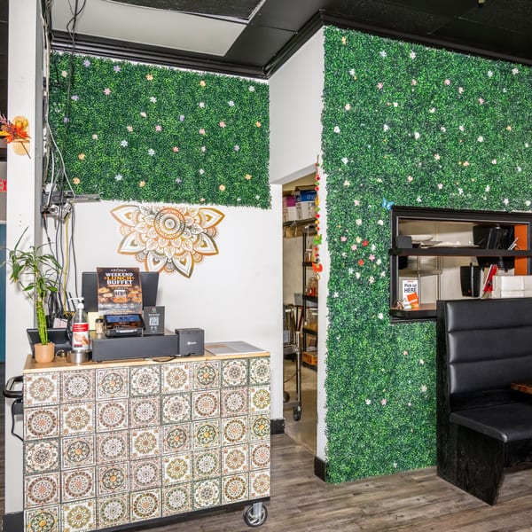 Restaurant interior with a decorative tiled counter, green plant walls, and a black booth.
