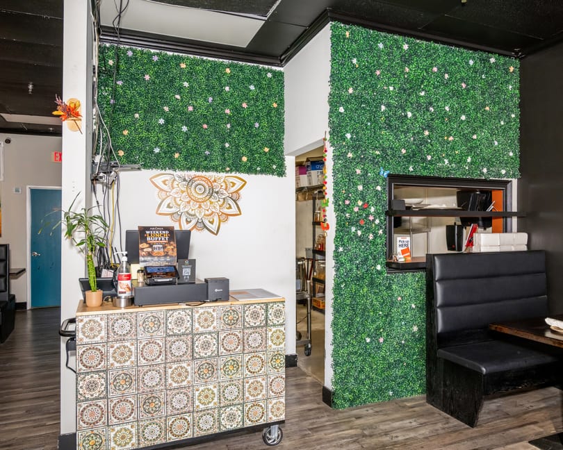 Restaurant interior with a decorative tiled counter, green plant walls, and a black booth.